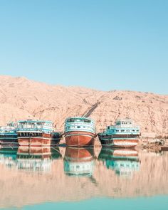 three boats are sitting in the water near some mountains