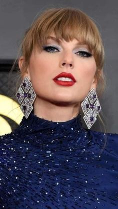 taylor swift wearing red lipstick and blue eyeshadow with large earrings on her head