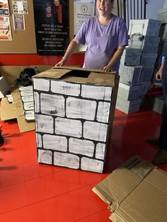 a man standing next to a cardboard box made out of bricks on top of a red floor