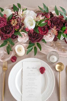 the table is set with white plates and silverware, red flowers, and candles