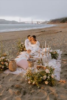 Bride and groom sitting at beach picnic with beautiful flowers and pink decorations at sunset Boho Beach Elopement, Elopement Picnic, Romantic Beach Picnic, Picnic Engagement