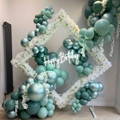 a happy birthday balloon arch decorated with white and blue balloons, flowers and greenery