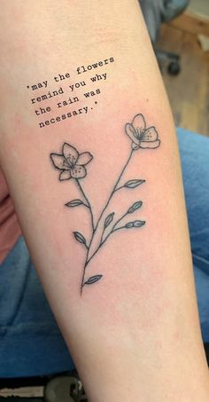 a woman's arm with a quote on it and flowers in the foreground