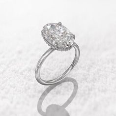 an oval shaped diamond ring sitting on top of a white surface with the reflection of it's center stone