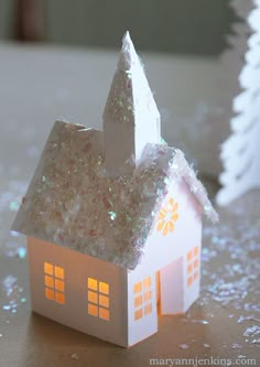 a small white house with snow on the ground next to a christmas tree and other decorations