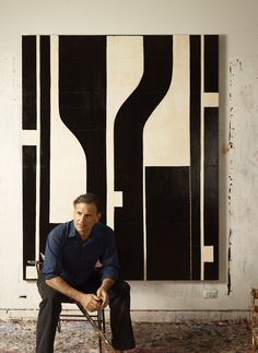 a man sitting on a chair in front of a large black and white piece of art