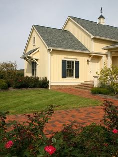 a yellow house with blue shutters and red brick walkway leading to the front door