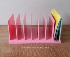 a pink desk organizer with cards and folders in it on a wooden table next to a white wall