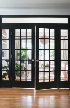 an empty room with black doors and wood flooring on the wooden floor is seen through glass windows