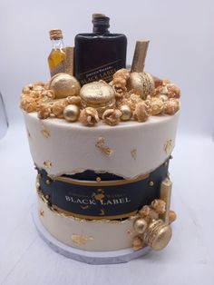 a white cake with gold decorations and bottles on the top is sitting on a table