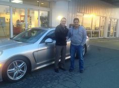 two men standing next to a silver sports car