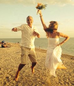 a man and woman are running on the beach with flowers in their hands as they dance