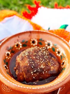 a meat dish with sesame seeds and sauce in a brown bowl on an orange table cloth