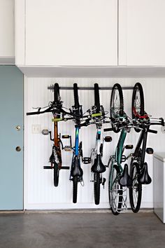 several bicycles are hanging on the wall in front of a blue door and white cabinets