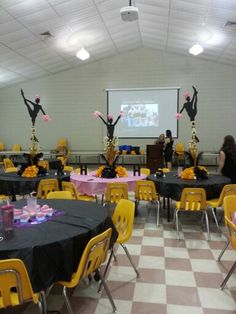 a room filled with tables covered in black tablecloths and yellow chairs, while two women are standing at the front of the room