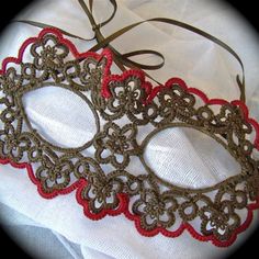 a pair of red and brown lace eye mask on a white cloth with a ribbon