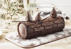 a log with pine trees on it sitting on a table next to wine glasses and flowers