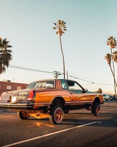 an orange pick up truck parked in a parking lot with palm trees and buildings behind it