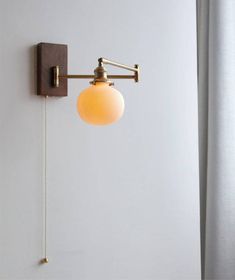 a wall mounted light on the side of a white wall next to a window with curtains