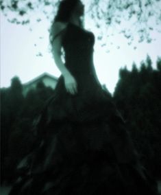 a woman in a black dress standing on top of a hill with trees behind her