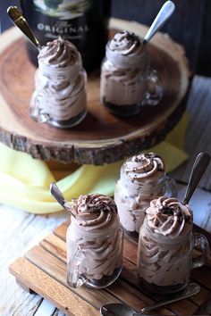 three desserts with chocolate frosting and spoons on a wooden tray next to a bottle