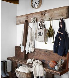 a wooden bench with several coats hanging on the wall and two clocks above it, along with other items