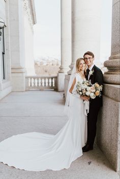 a bride and groom pose for a photo in front of the columns on their wedding day