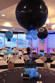 black and blue balloons are on top of a round table in the middle of a banquet hall