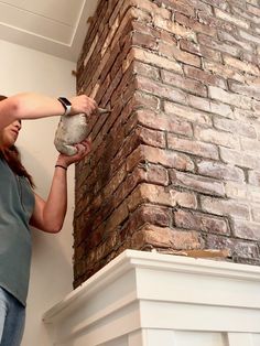 a woman is painting a brick wall with white paint