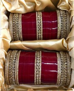 two red and gold bangles are sitting in a box with satin material on it