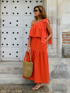 a woman in an orange dress holding a straw bag