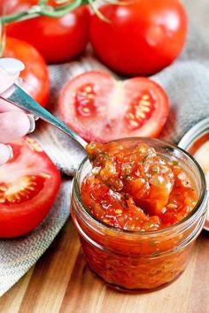 a jar filled with tomato sauce on top of a wooden table next to sliced tomatoes