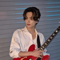 a young man holding a red guitar in his right hand and wearing a white shirt