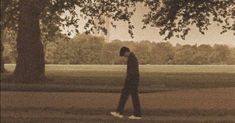 a man walking through a park with trees in the background