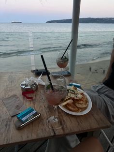 two people sitting at a table with food and drinks on it, overlooking the ocean