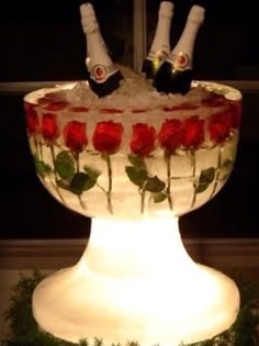 two bottles of champagne sitting on top of a glass bowl filled with ice and roses