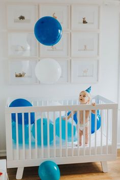 a baby in a white crib with balloons and blue balls hanging from the ceiling