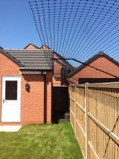 an outdoor area with a fence, grass and a brick house in the back ground