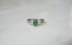 an emerald and diamond ring sits on a marble surface