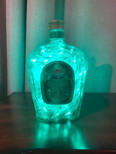 an illuminated bottle sitting on top of a wooden table in front of a green curtain