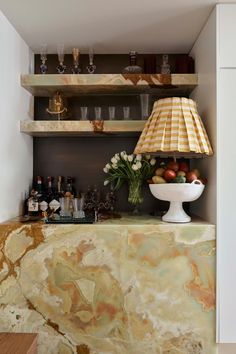 a kitchen with marble counter tops and shelves filled with bottles, glasses, vases and flowers