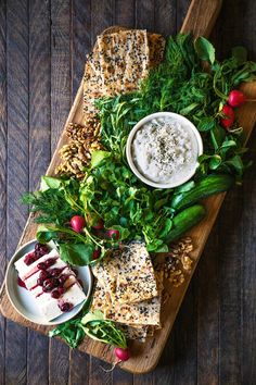 a wooden platter filled with greens and dips next to crackers on a table