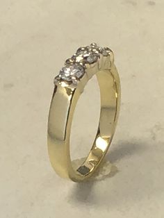 a yellow gold ring with three diamonds on the top and bottom, sitting on a white surface