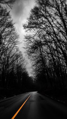 an empty road surrounded by trees with no leaves on the side and dark clouds in the background