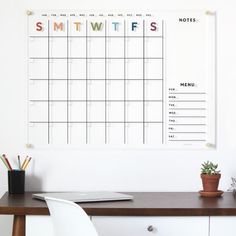 a desk with a calendar on it next to a potted plant and pencils