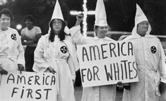 four women in white robes holding signs with american first written on them while standing next to each other