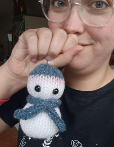 a woman wearing glasses is holding a knitted snowman ornament in front of her face