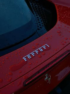 the hood of a red sports car with water droplets on it