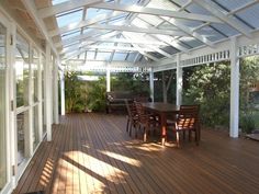 a wooden deck with chairs and table under a glass roof