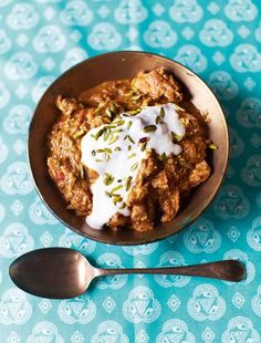 a bowl filled with food next to two spoons on top of a blue tablecloth